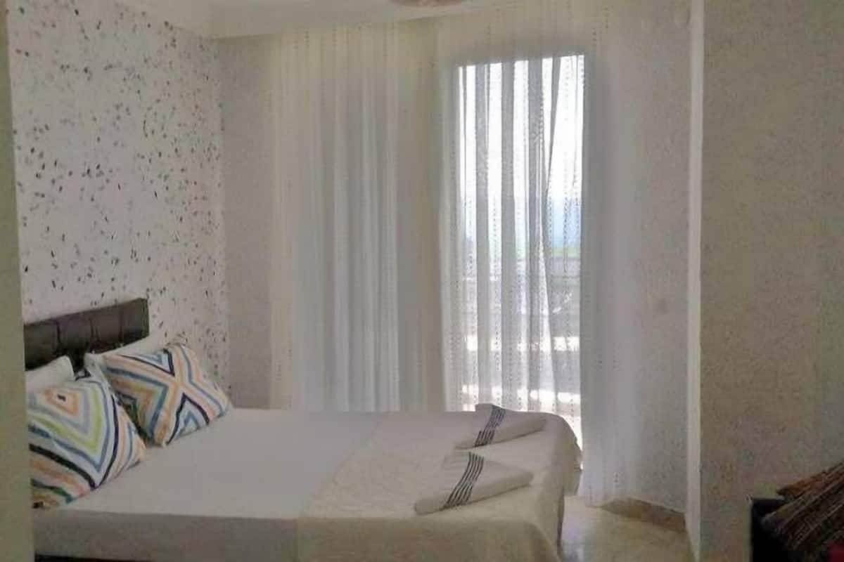 A hotel room with a bed, a window with curtains, and a view of the outdoors.