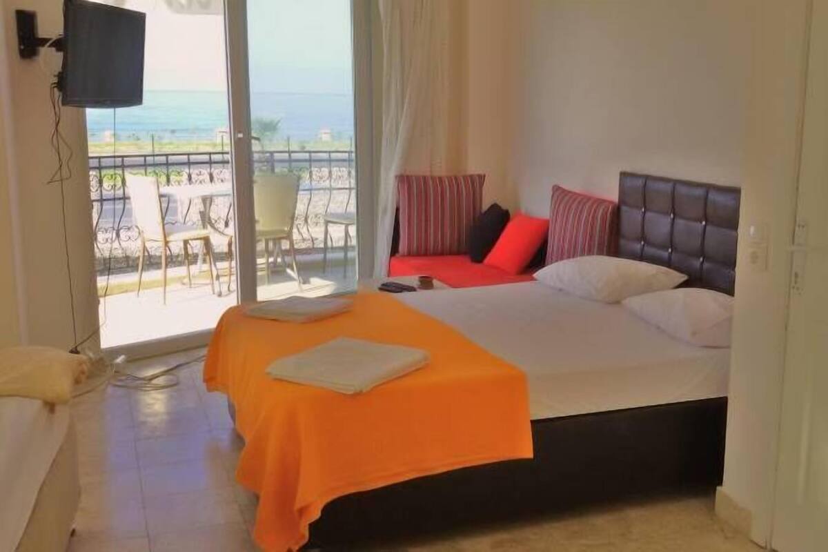 A hotel room with a bed, a TV, and a balcony with a view of the sea.