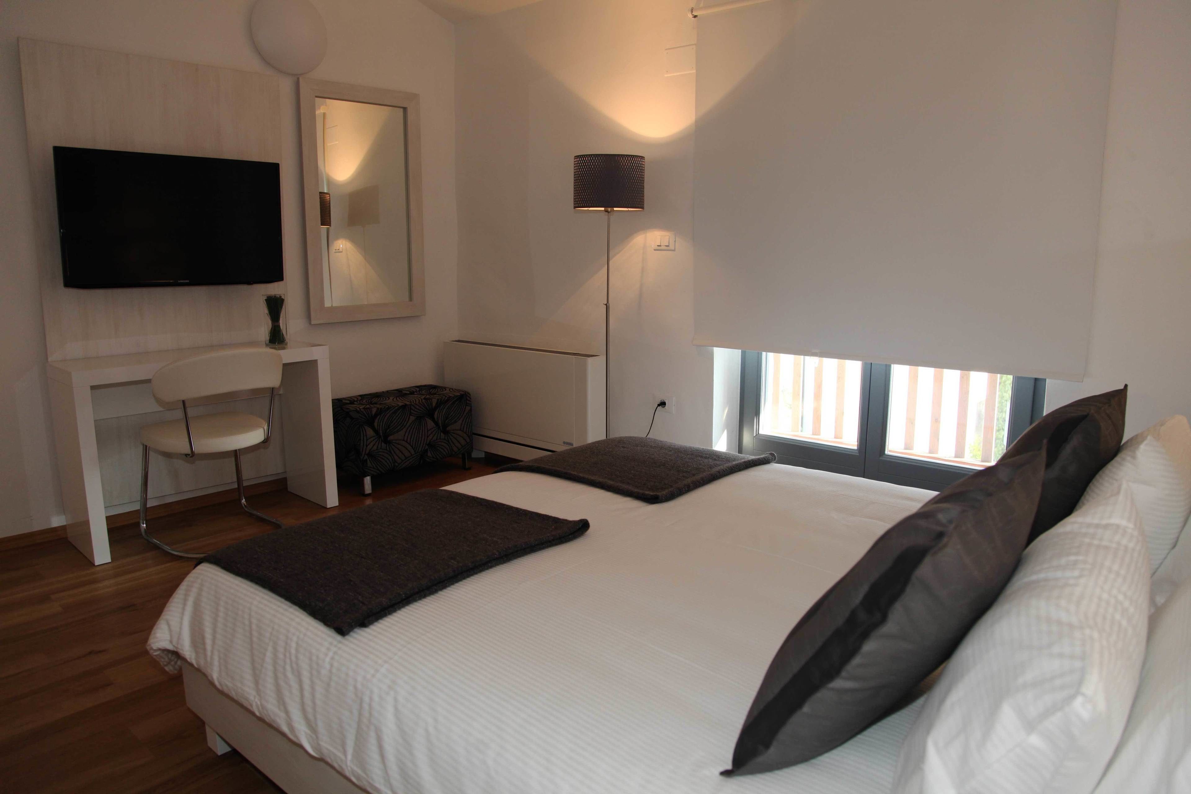 Un dormitorio moderno con una cama grande, un televisor de pantalla plana en la pared, un escritorio con una silla y una lámpara de pie.