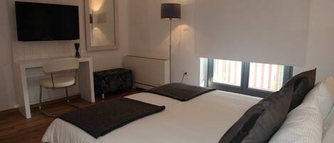 Un dormitorio moderno con una cama grande, un televisor de pantalla plana en la pared, un escritorio con una silla y una lámpara de pie.