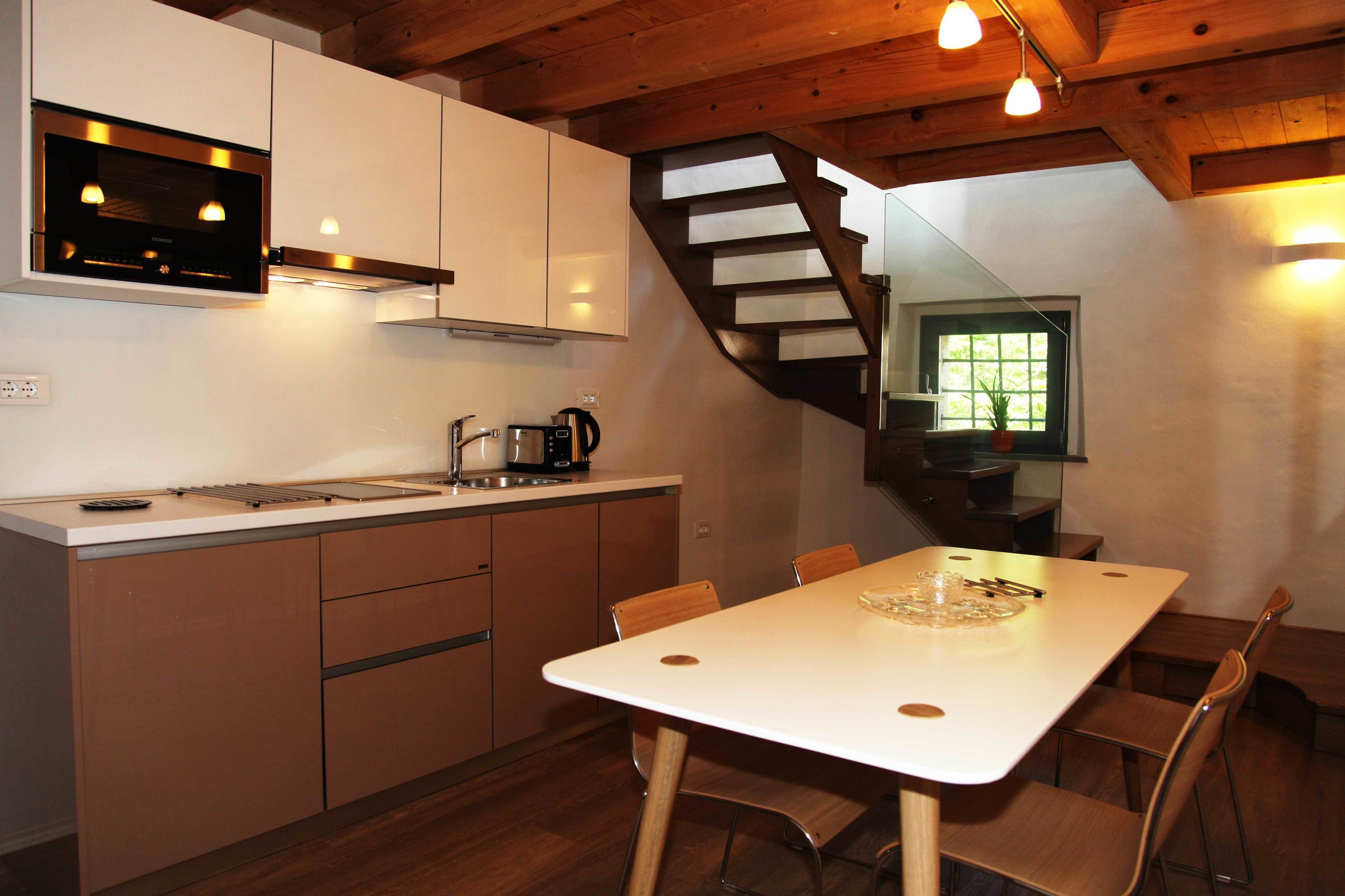 A modern kitchen with white cabinets, a wooden staircase, and a dining area with a white table and chairs.