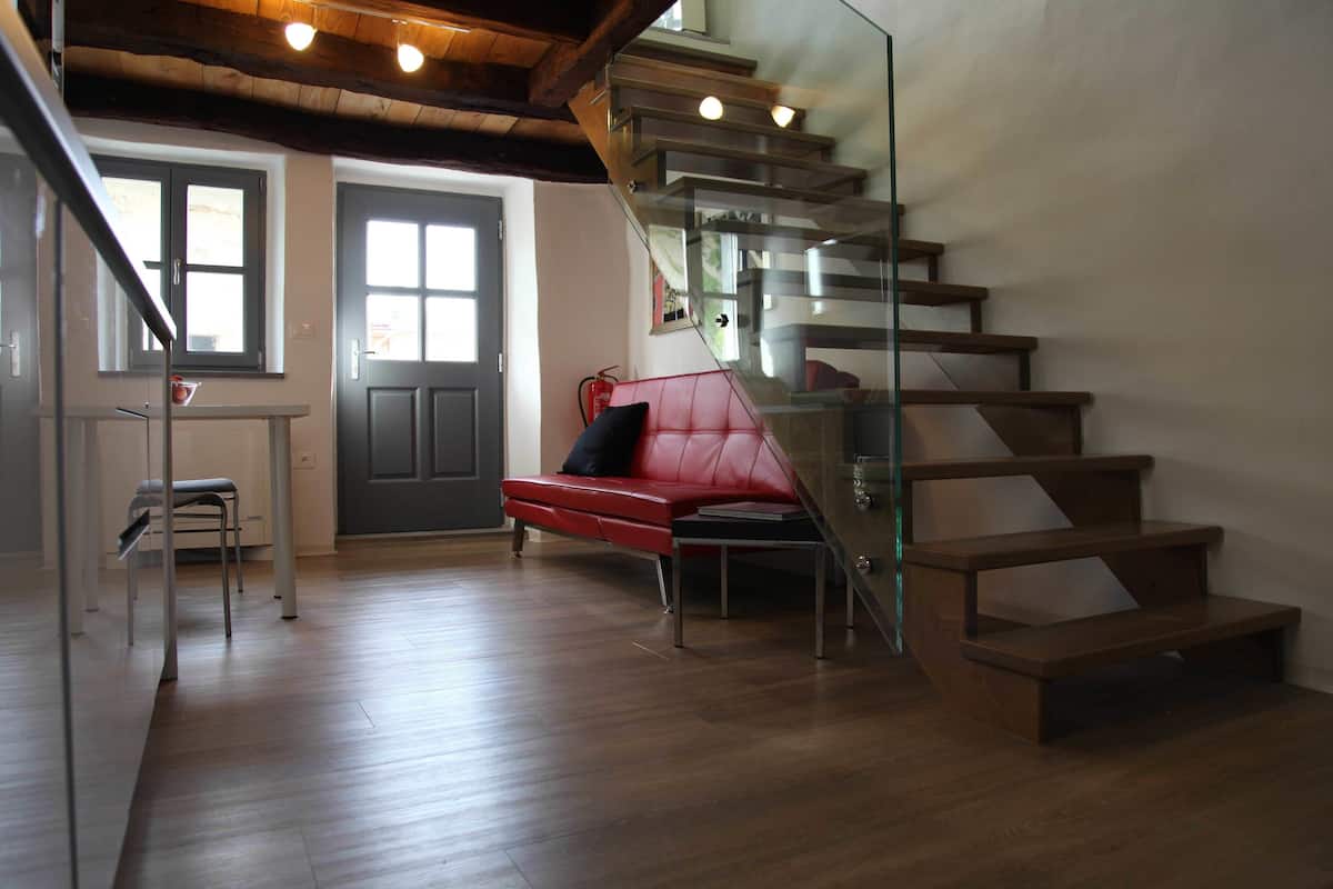 A modern interior with a wooden staircase, a red sofa, and a glass railing.