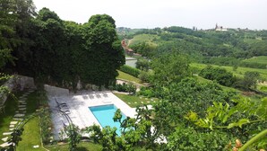A pool area with lounge chairs, surrounded by lush greenery and a view of rolling hills and a distant building. - Boutique Hotel Dvor (Brda)