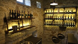 A bar area with shelves of wine bottles, a sink, and two bar stools. - Boutique Hotel Dvor (Brda)