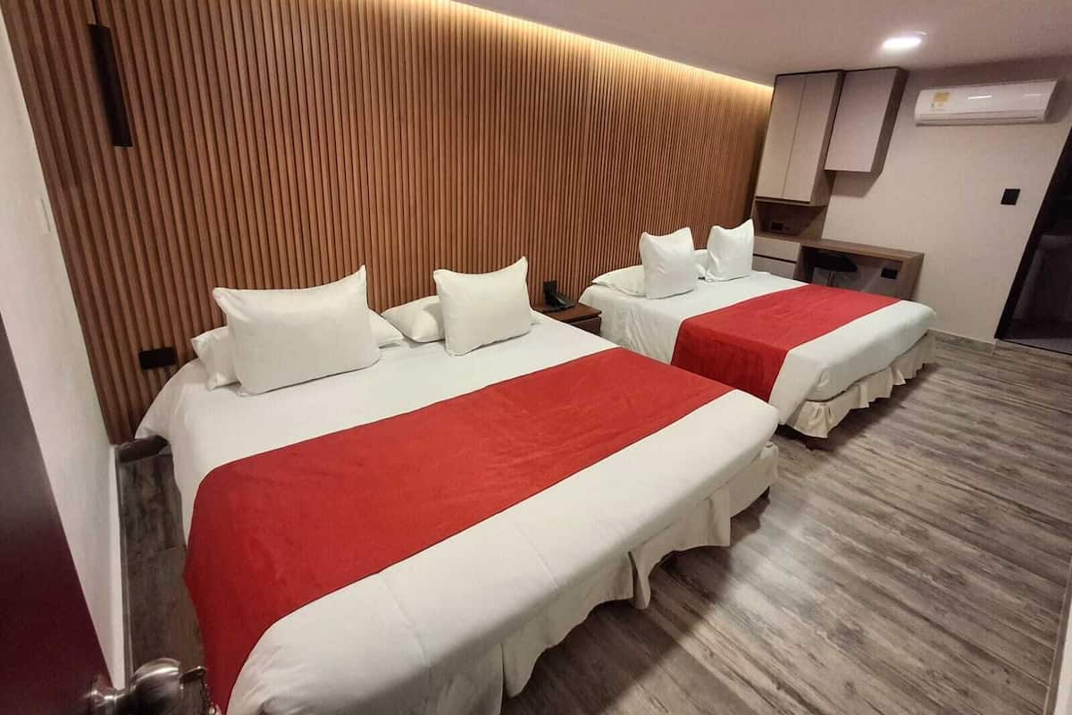 Ein Hotelzimmer mit zwei Betten, jeweils mit weißer Bettwäsche und roten Akzenten, einem Holz-Schrankbett, einem kleinen Schreibtisch mit Stuhl und einer Wand-Klimaanlage.