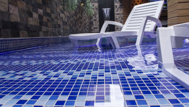 A swimming pool with blue mosaic tiles, a white lounge chair, and a stone wall. - Hotel León Dorado (Bucaramanga)