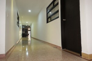 A hallway with a polished floor, a black door, and a window with blinds.