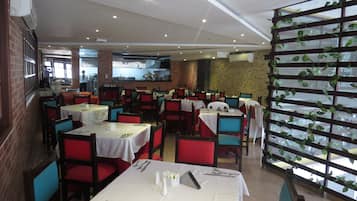 A restaurant with multiple tables and chairs, a kitchen area, and a brick wall.