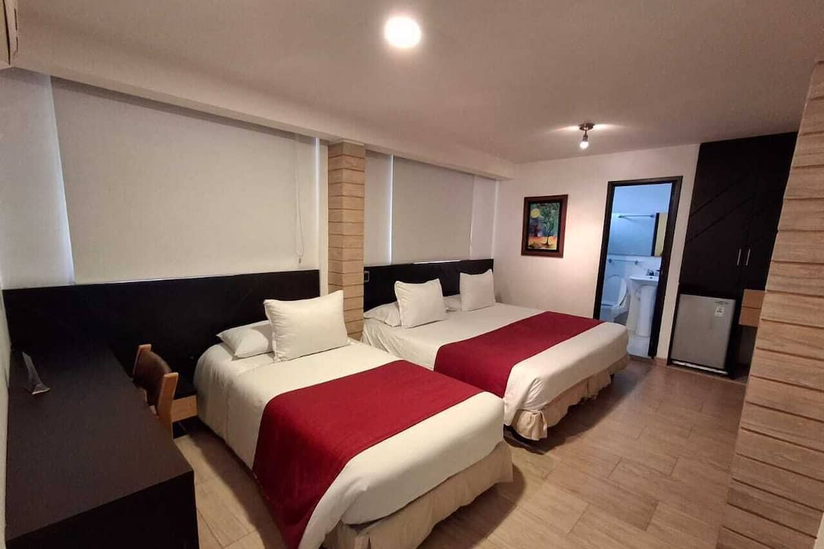 Ein Hotelzimmer mit zwei Betten, einem Schreibtisch, einer kleinen Küchenzeile und einem durch eine geöffnete Tür einsehbaren Badezimmer.