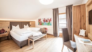 A modern hotel room with a wooden headboard bed, a bench, a desk, and a large window with curtains. - Appartement Ausserladscheider (Leutasch)