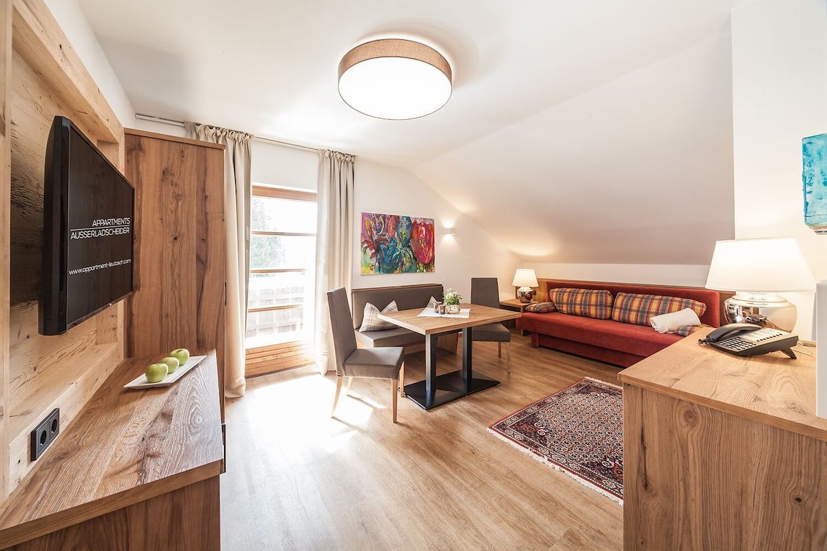 Un appartement moderne comprenant un coin repas, un canapé, un téléviseur fixé au mur et une grande fenêtre.