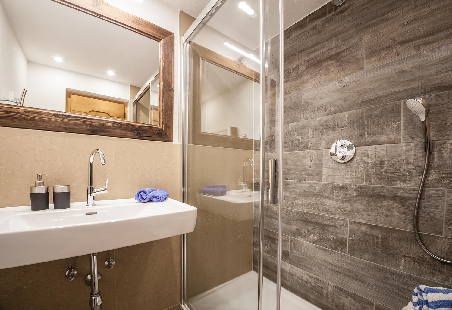 A modern bathroom with a glass shower enclosure, a white sink with a mirror above it, and wooden wall tiles.