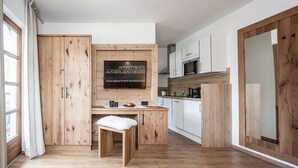A modern kitchen with wooden cabinetry, a built-in stove, and a dining area with a white chair. - Appartement Ausserladscheider (Leutasch)