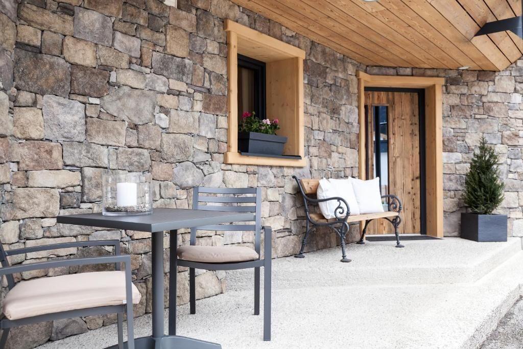 A stone exterior with a wooden door, a bench, and a table with cushions.