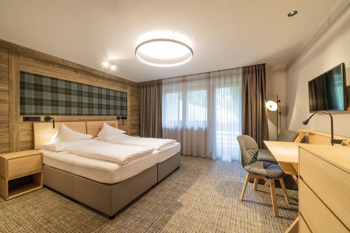 A hotel room with a large bed, a desk, a chair, a TV, and a window with curtains.