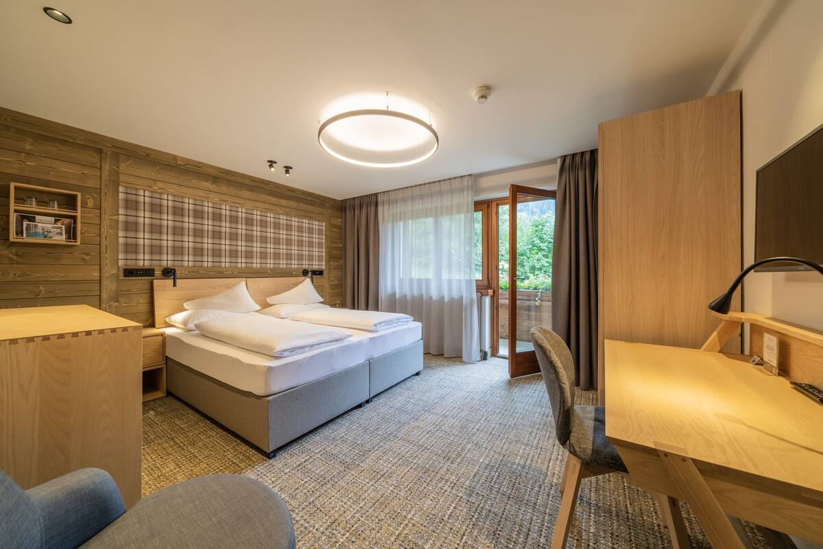 A hotel room with a bed, a desk, a chair, a wardrobe, and a window with curtains.