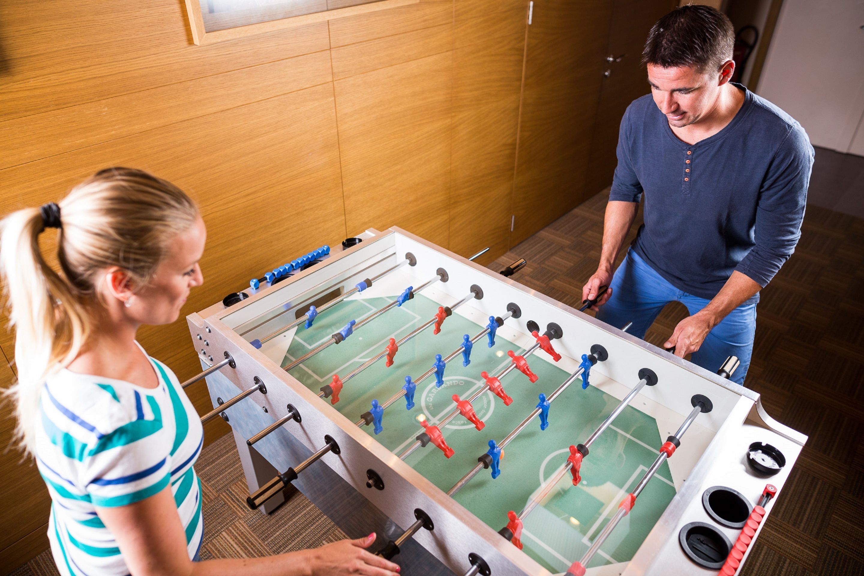 A foosball table in a room with wooden paneling and a door in the background.