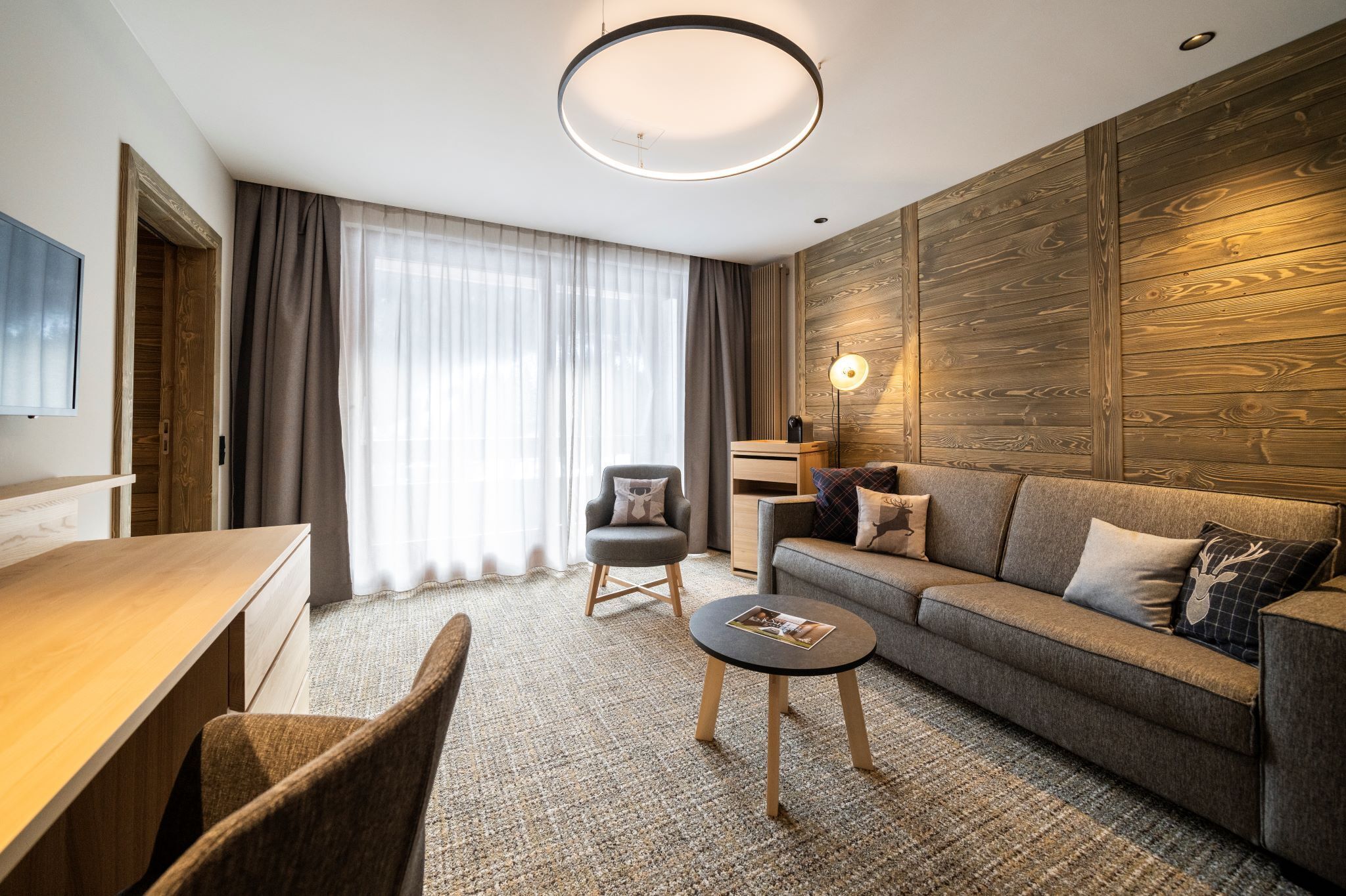 A modern living room with a sofa, armchair, coffee table, and a TV on a wooden wall.