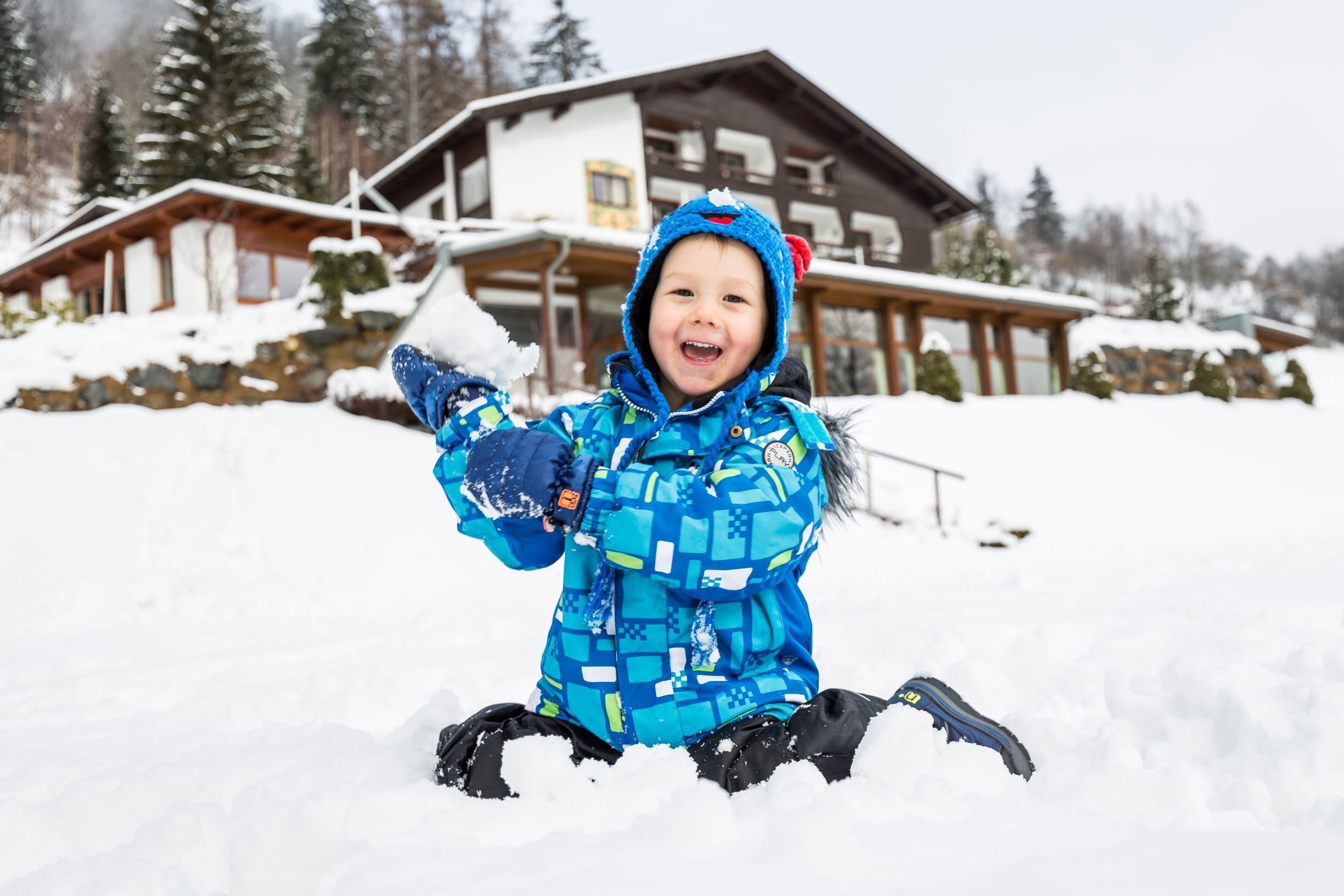 Un niño jugando en la nieve con una cabaña de madera al fondo.