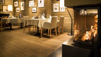 Un restaurant chaleureux avec des planchers, des tables et des chaises en bois, et des tableaux encadrés accrochés aux murs. On aperçoit une cheminée au premier plan.