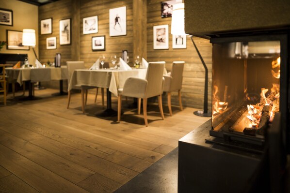 Un restaurant chaleureux avec des planchers, des tables et des chaises en bois, et des tableaux encadrés accrochés aux murs. On aperçoit une cheminée au premier plan.