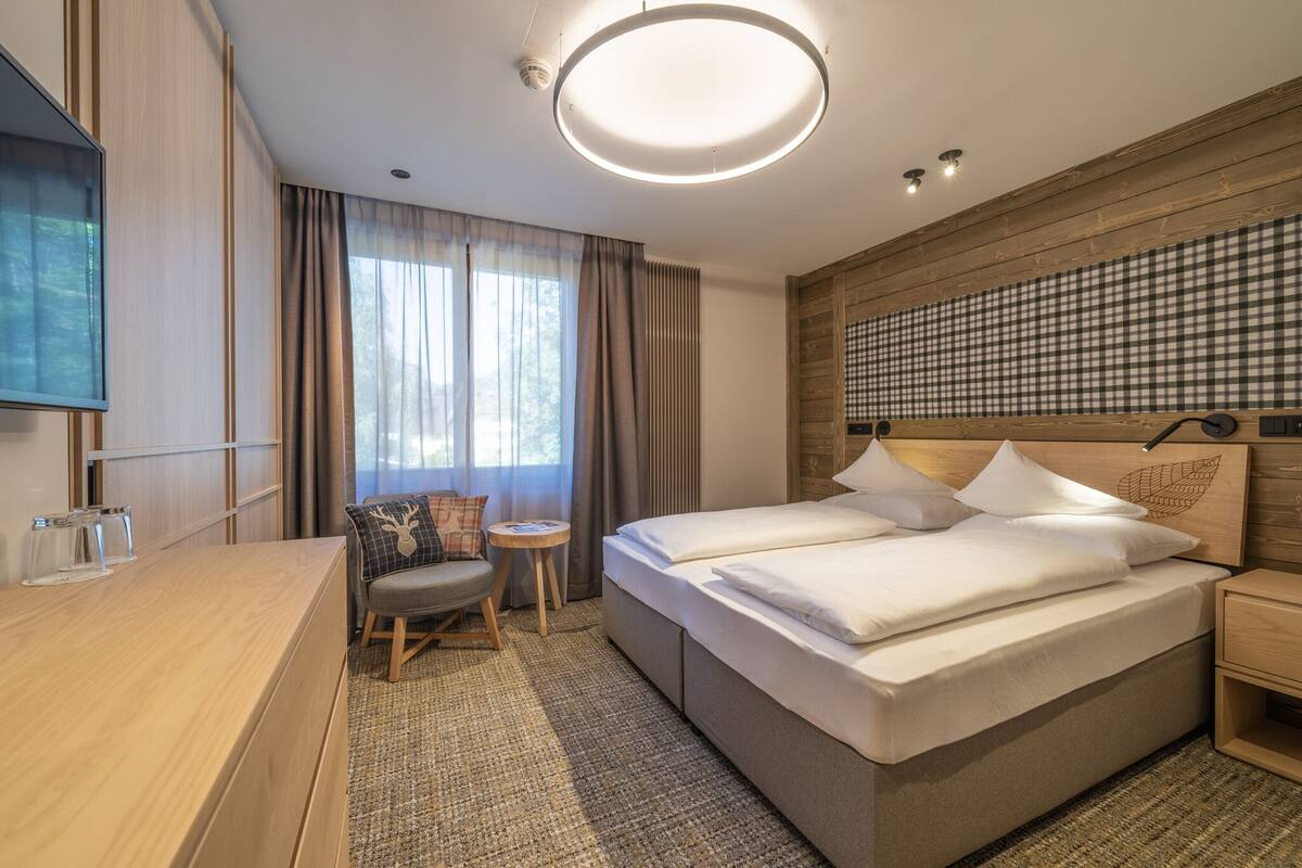 A modern hotel room with a large bed, a desk, a chair, and a small table.