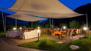 An outdoor dining area with tables and chairs under a large canopy, set against a mountainous backdrop. - Hotel OTP Birkenhof (Bad Kleinkirchheim)