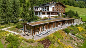A large hotel with multiple floors, a rooftop terrace with lounge chairs, and a lush garden. - Hotel OTP Birkenhof (Bad Kleinkirchheim)