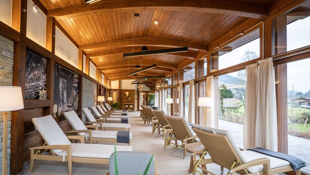 A sunlit lounge area with wicker furniture, large windows, and a wooden ceiling. - Hotel OTP Birkenhof (Bad Kleinkirchheim)