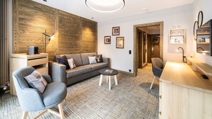 A modern living room with a sofa, armchairs, a coffee table, and a wooden accent wall. - Hotel OTP Birkenhof (Bad Kleinkirchheim)