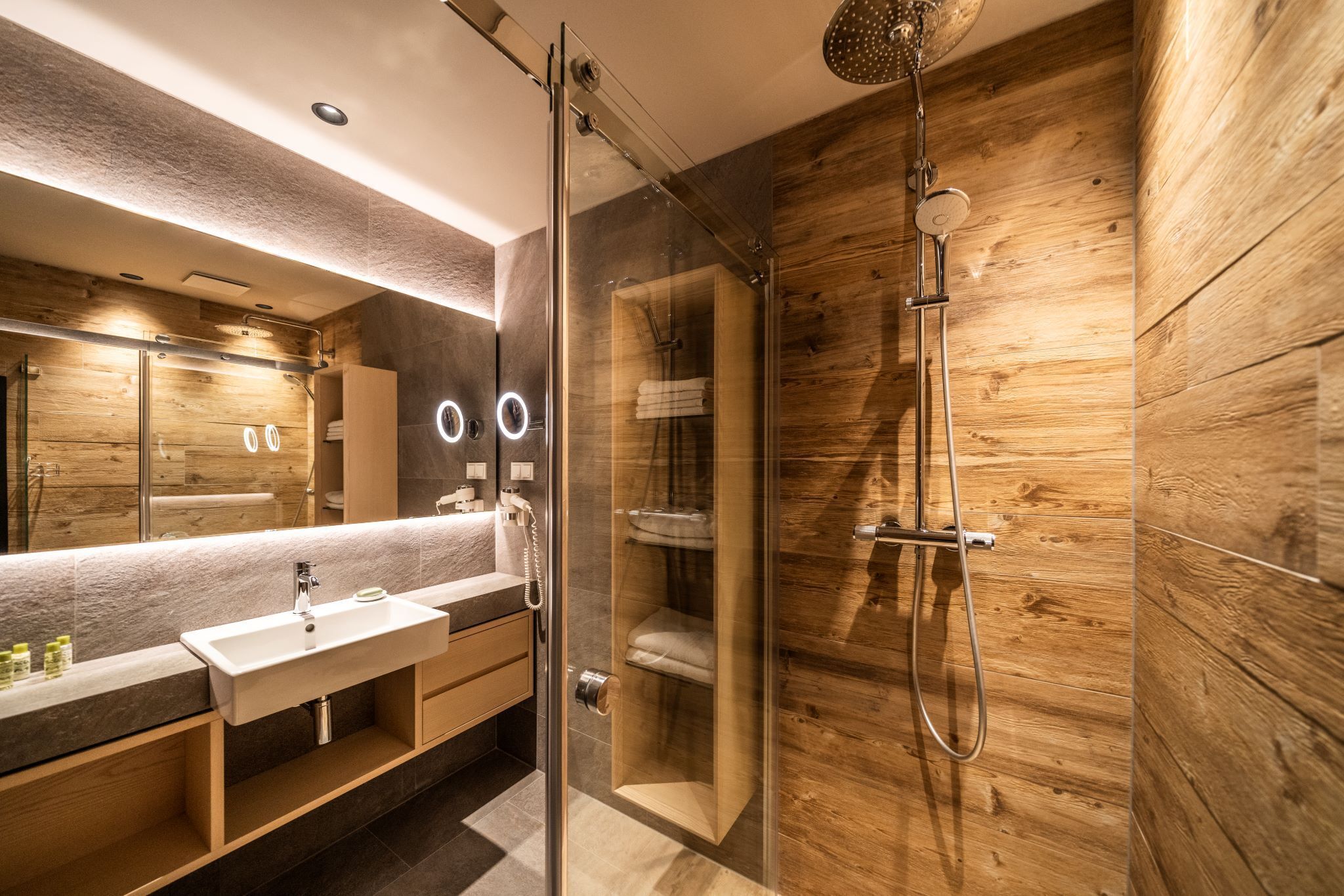 A modern bathroom with a glass-enclosed shower, a vanity with a sink, and a large mirror.