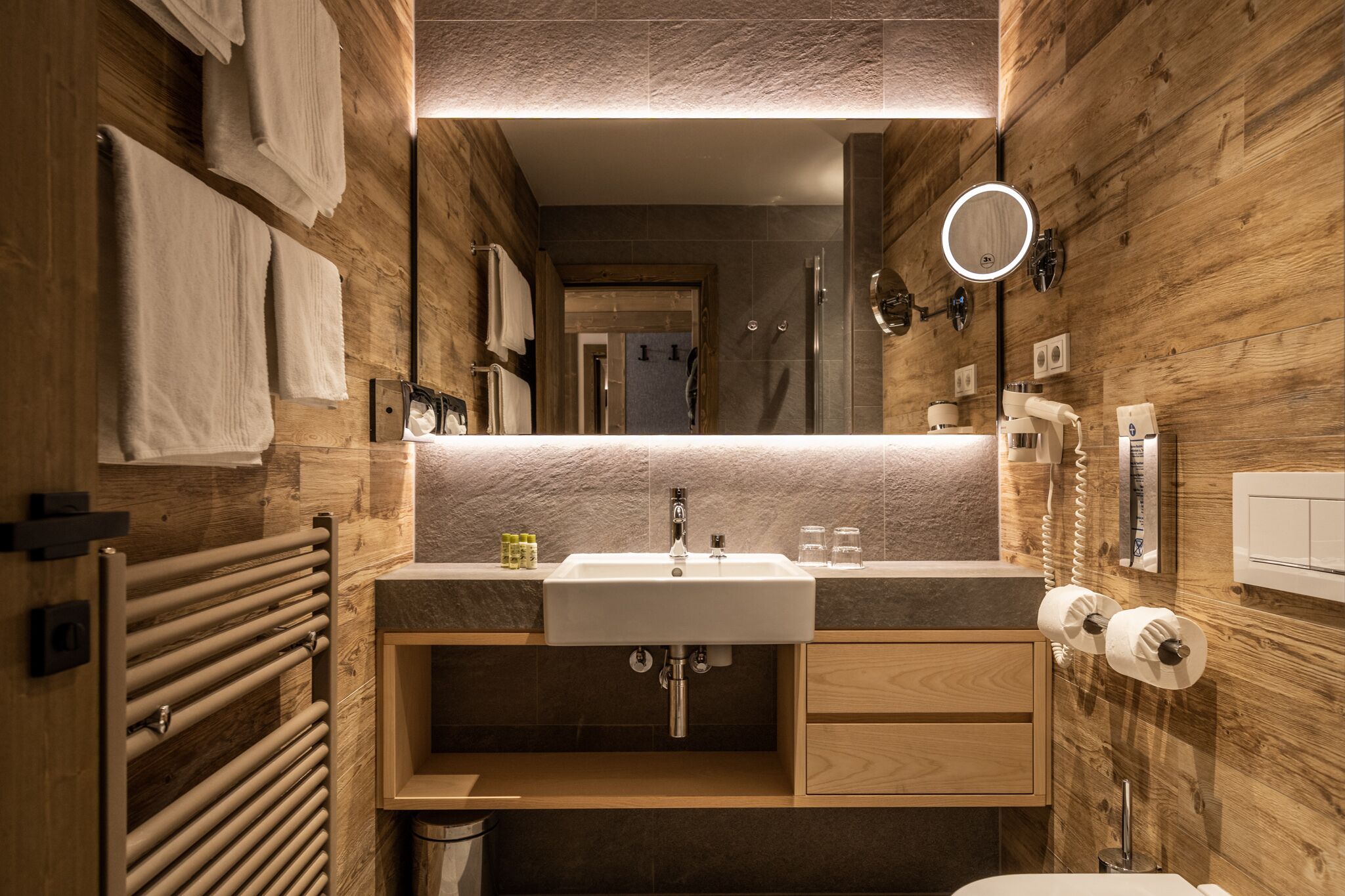 A modern bathroom with a wooden wall, a sink, a mirror, and a towel rack.