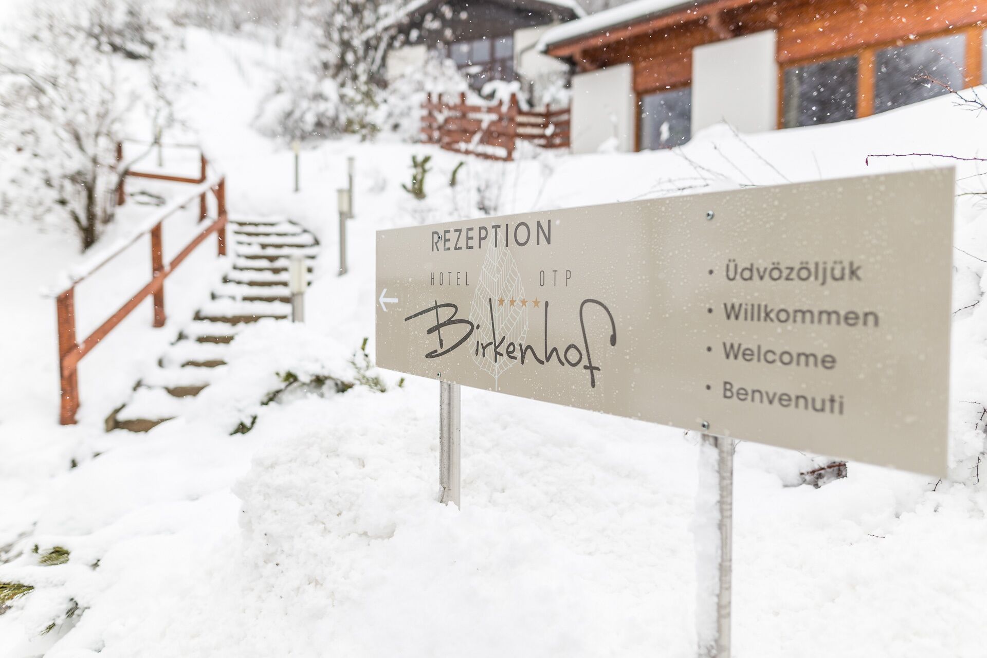 A reception sign with multilingual welcome messages in a snowy setting.