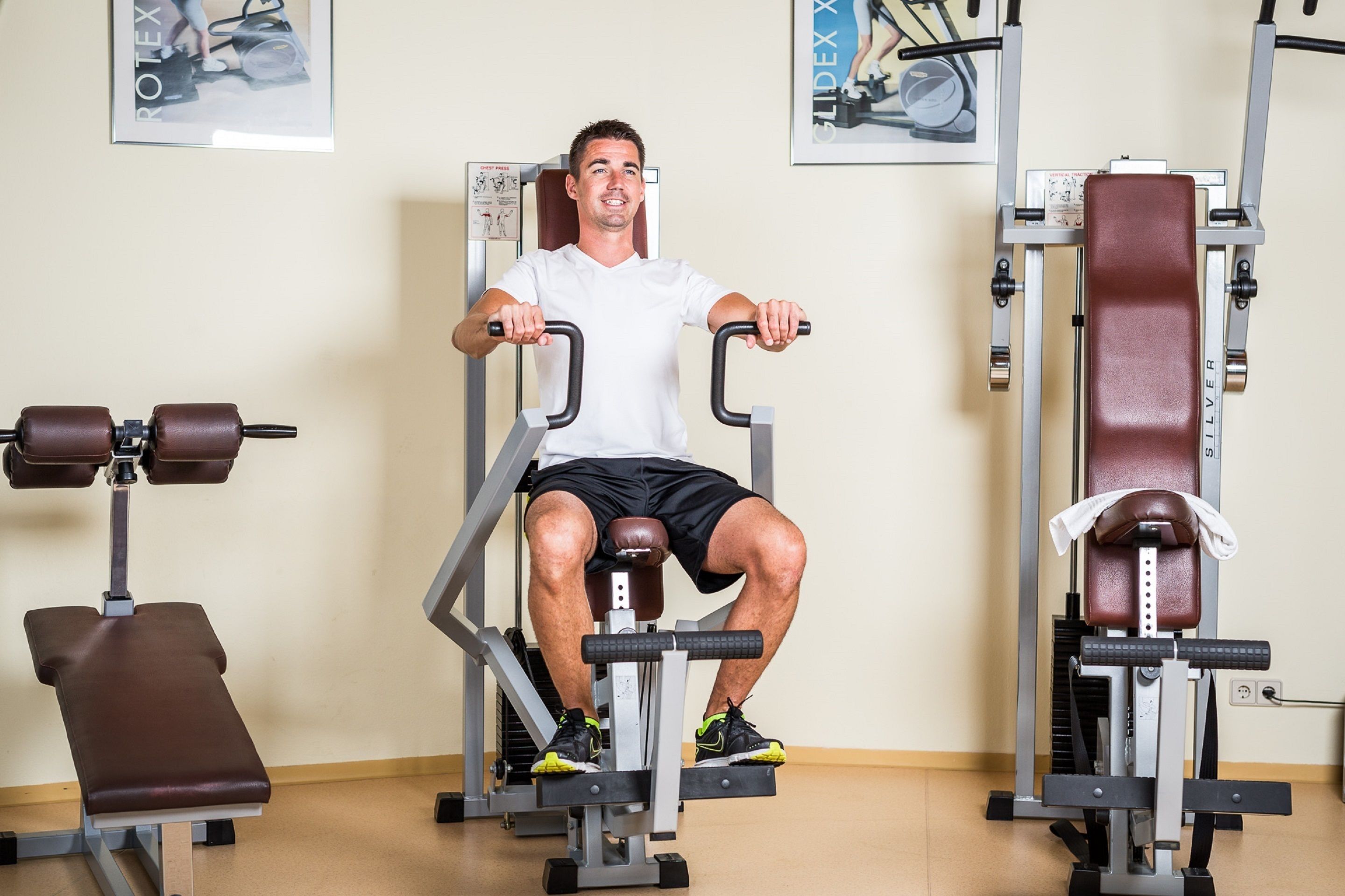 Un uomo utilizza una macchina per lo sviluppo delle gambe in palestra, circondato da altre attrezzature da allenamento.