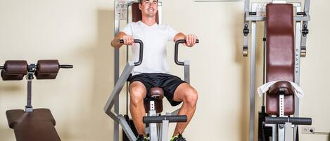 A man using a leg press machine in a gym with various other exercise equipment around.