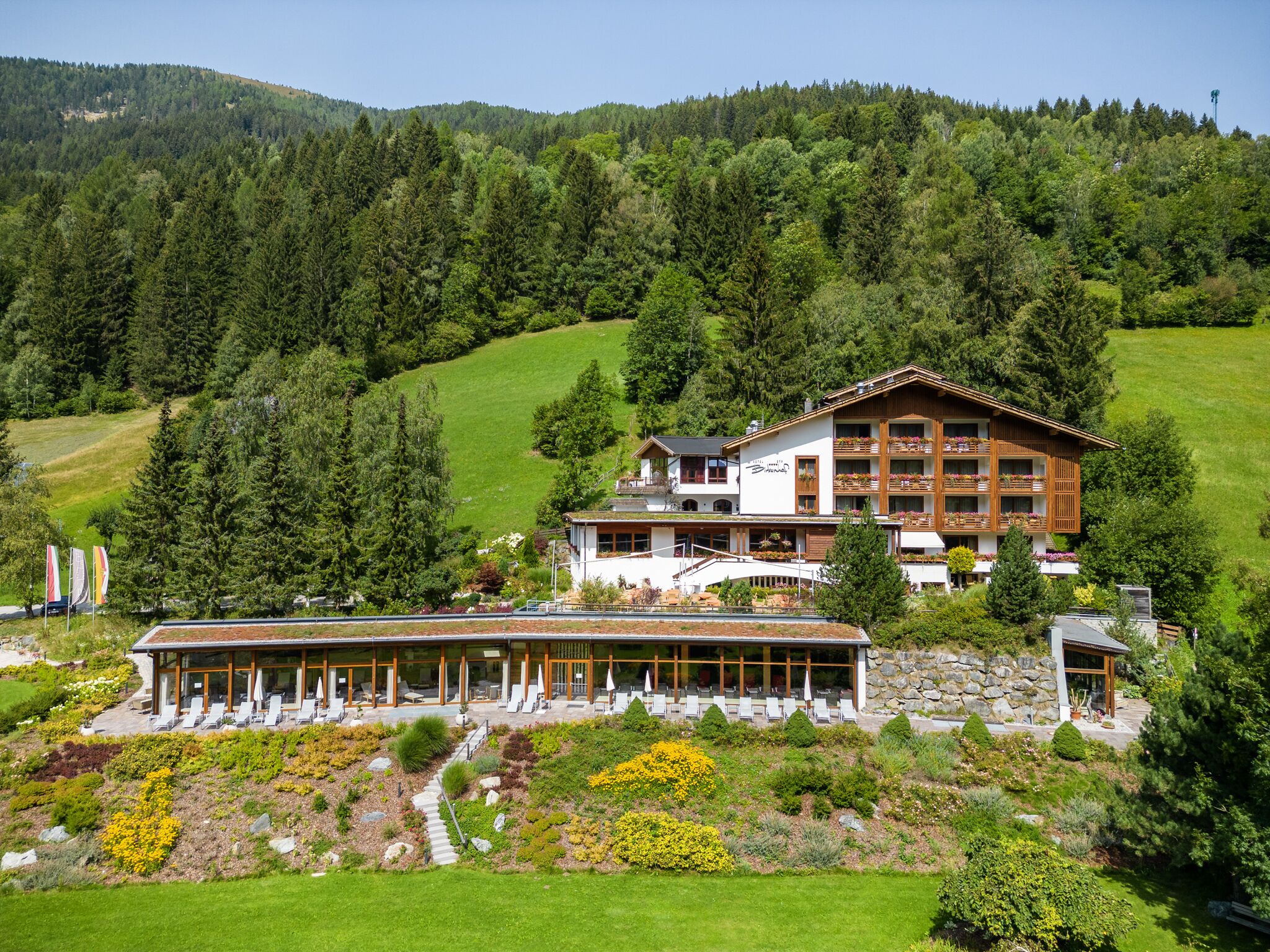A hotel with a large building and a smaller annex, surrounded by lush greenery and a mountainous backdrop.