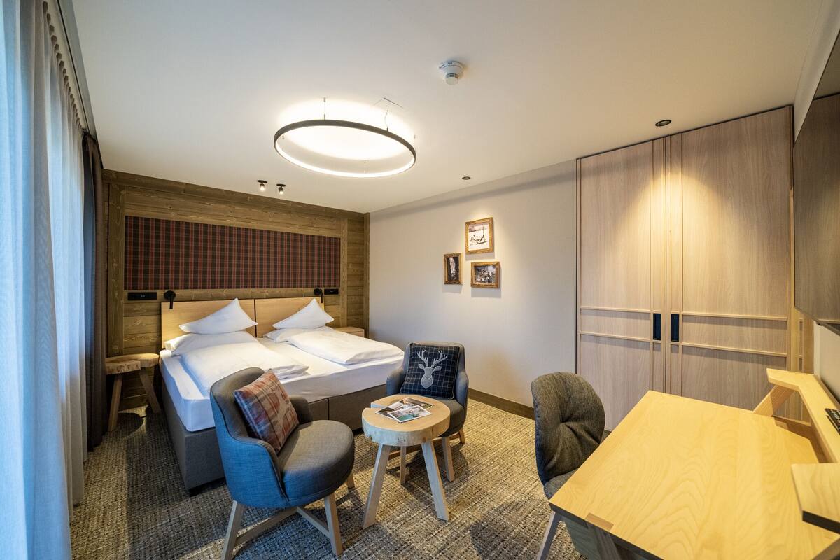 A hotel room with a bed, two chairs, a small table, a wooden desk, and a wardrobe.