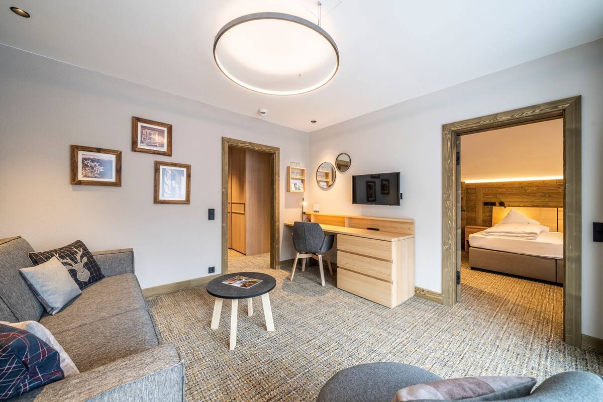 A modern hotel room with a sofa, a small round table, a desk, a bed, and a TV.