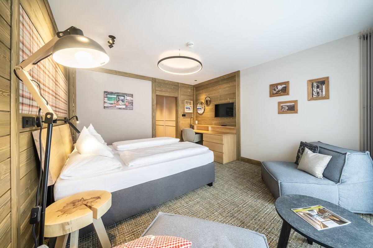 A hotel room with a bed, a desk, a sofa, a lamp, and a TV.
