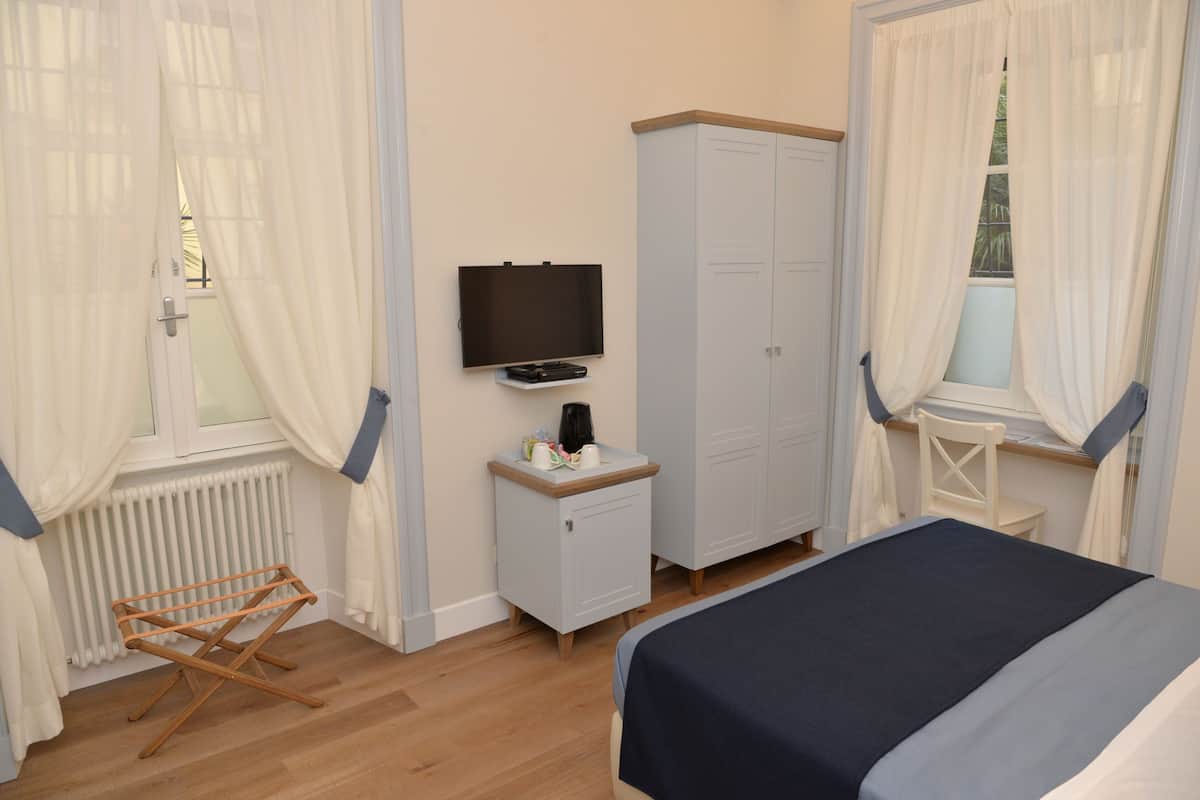 Un dormitorio con cama, televisor, armario, tendedero y ventana con cortinas.