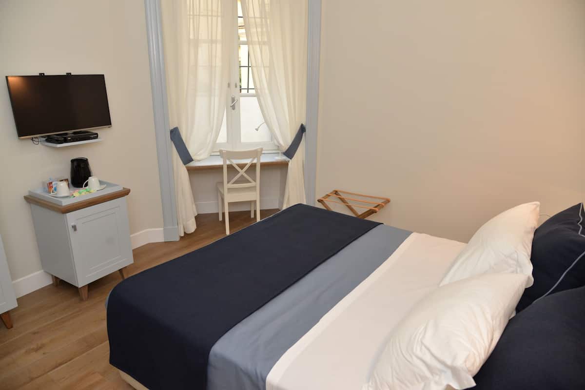 Una habitación de hotel con cama, escritorio, silla, televisor y un mueble pequeño.