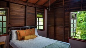 A wooden room with a bed, large windows, and a view of greenery outside. - Naniki Cottages (Surinam)