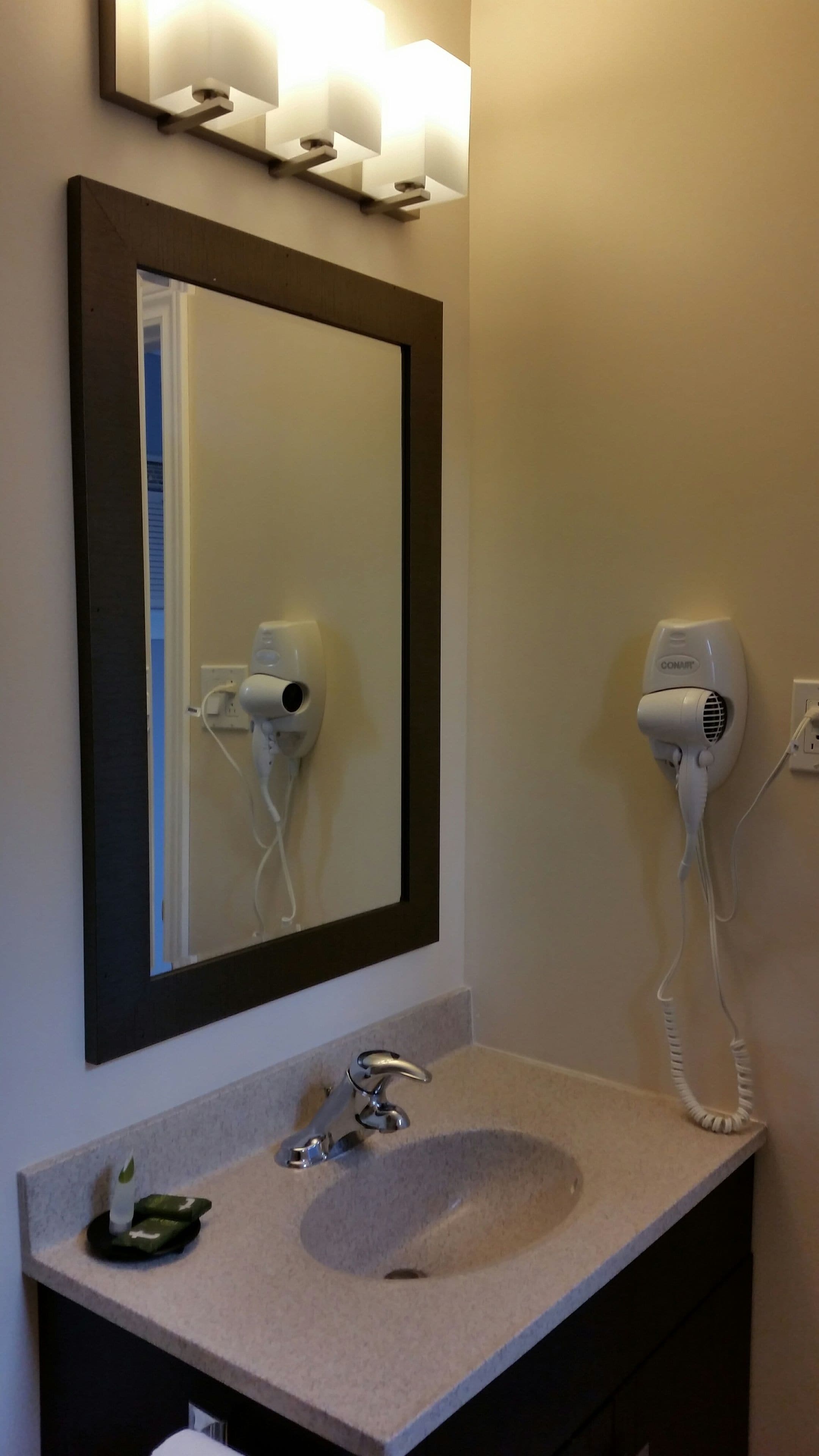 Un baño con lavabo, espejo y secador de pelo fijado a la pared.