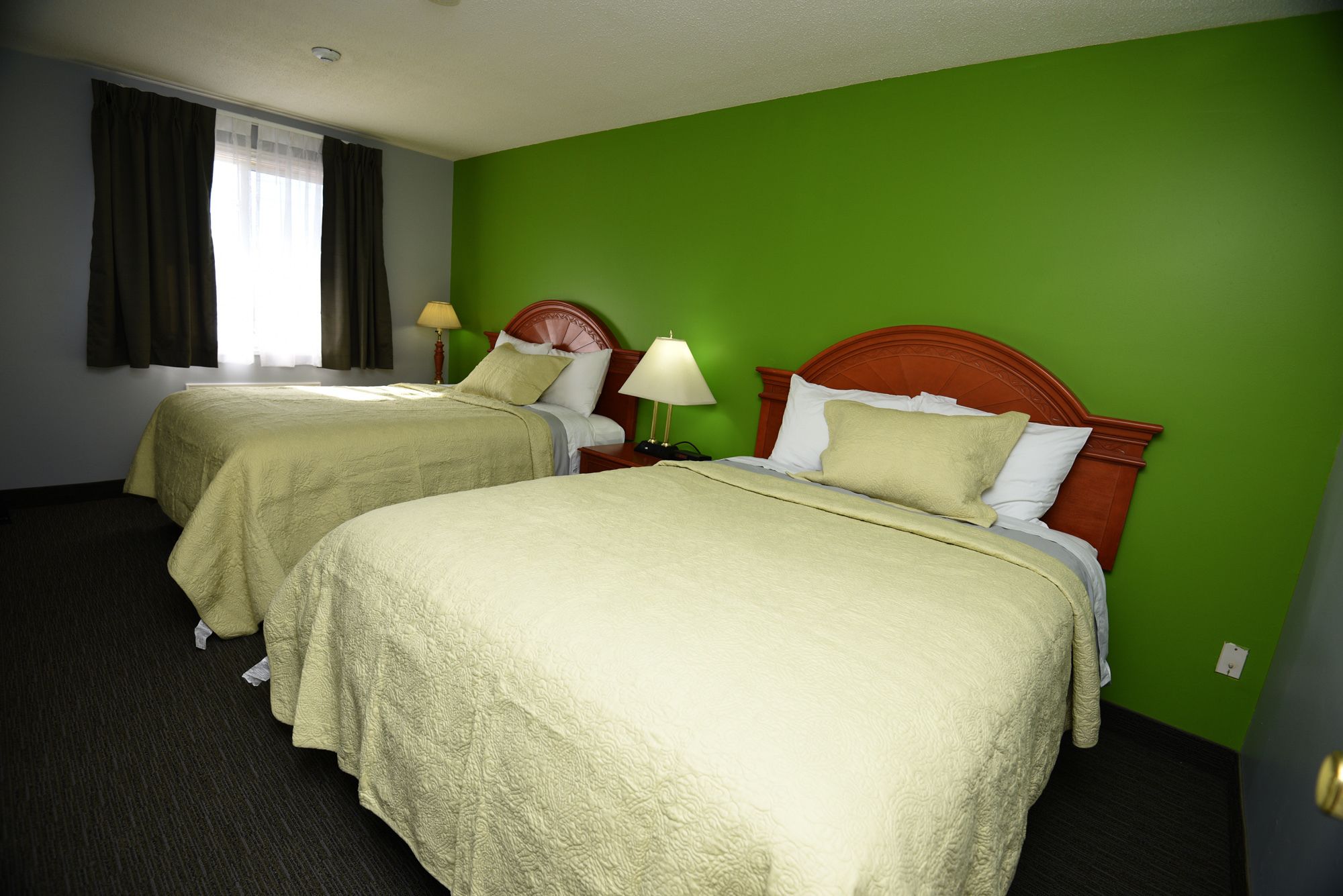 Ein Hotelzimmer mit zwei Betten, grünen Wänden und einem Fenster mit Vorhängen.