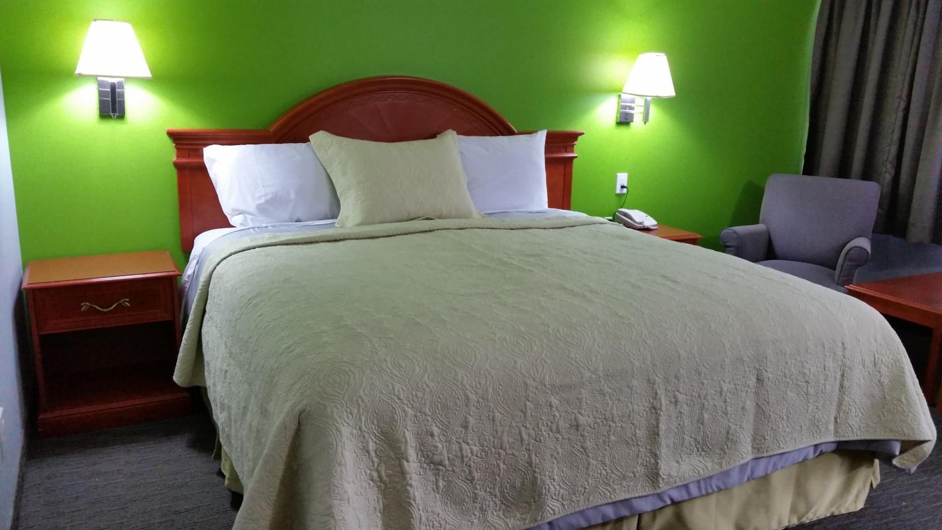 A hotel room with a bed, two bedside tables, a chair, and two wall-mounted lamps.