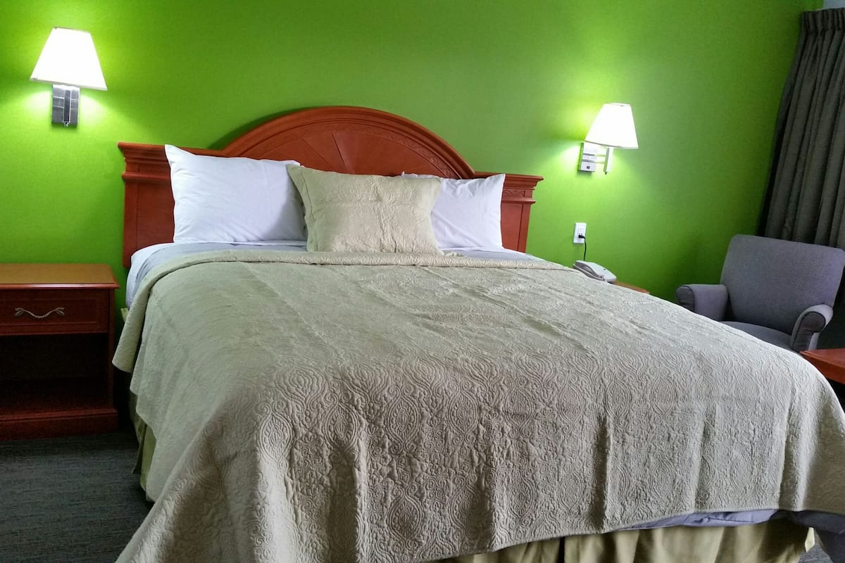 A hotel room with a bed, two bedside lamps, a nightstand, a chair, and a window with curtains.