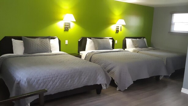A room with three beds, each with a headboard and pillows, against a green wall. There are two wall-mounted lamps on either side of the beds. - Nipissing Inn (North Bay)