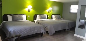 Habitación con tres camas, cada una con cabecera y almohadas, frente a una pared verde. Hay dos lámparas de pared a cada lado de las camas.