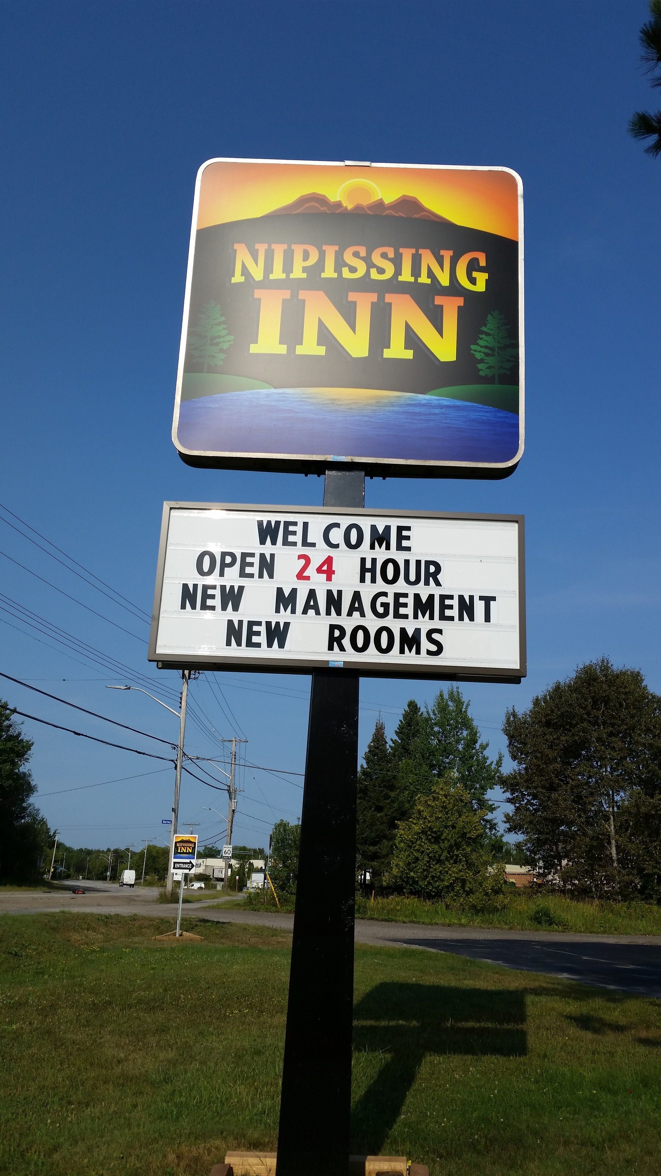 Placa do Nipissing Inn com um belíssimo pôr do sol ao fundo, dando as boas-vindas aos visitantes com atendimento 24 horas, nova administração e quartos renovados.