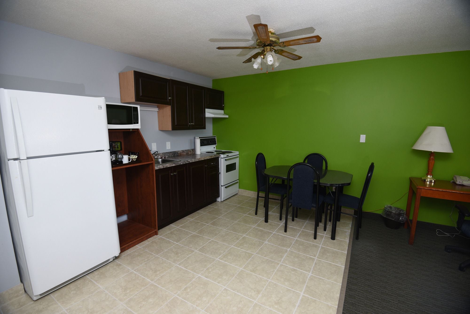 A compact kitchen with a refrigerator, microwave, stove, and cabinets. There is a dining area with a table and chairs.